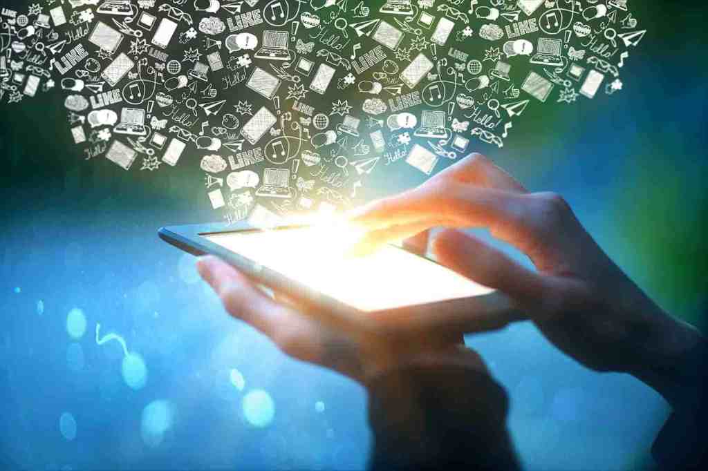 Hands holding tablet with communication icons Closeup of male hands holding and touching illuminated screen of digital tablet with abstract communication icons on blue background. Social media concept